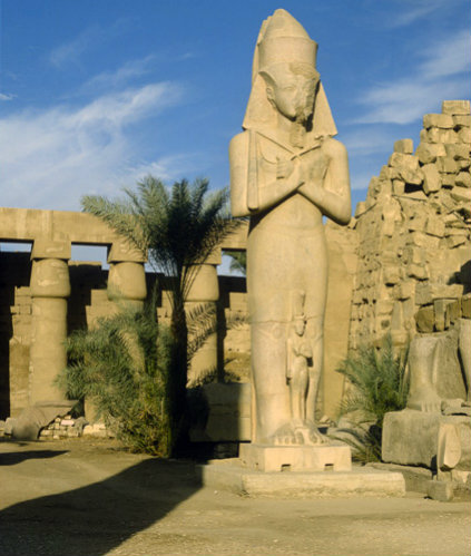 Colossal red granite statue of Ramesses II with his consort Nefertari standing between his knees, Karnak, Egypt