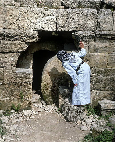 Arab looking into tomb past rolling stone, south west of Hebron, Israel