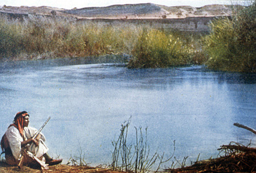 Arab sitting by the Jordan River holding a rifle, circa 1906, old postcard, Palestine