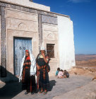 Two Berber women standing outside carved door of mausoleum, Takrouna, Tunisia
